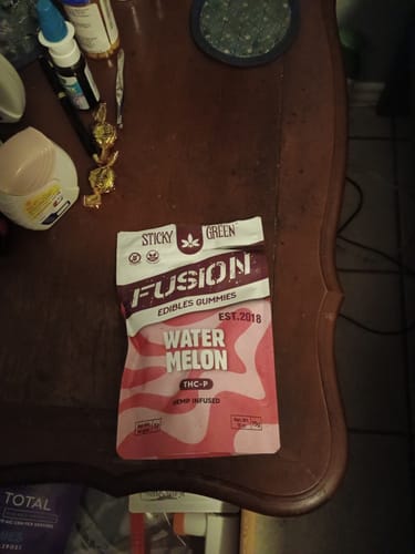 Customer's Watermelon Fusion Gummies pouch resting on a wooden table among other items.