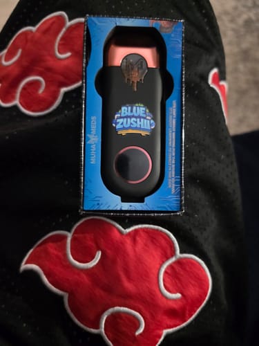 Customer's Blue Zushi MUHA Meds Melted Diamonds vape pen in its black and blue box, held against patterned fabric.