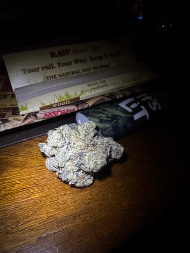 Customer's dense, trichome-covered Cereal Milk THCA flower bud resting on a wooden surface next to rolling papers.