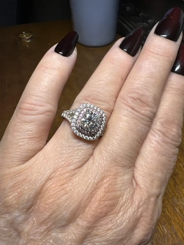 Customer's square-cut engagement ring with a paved halo setting worn on a finger