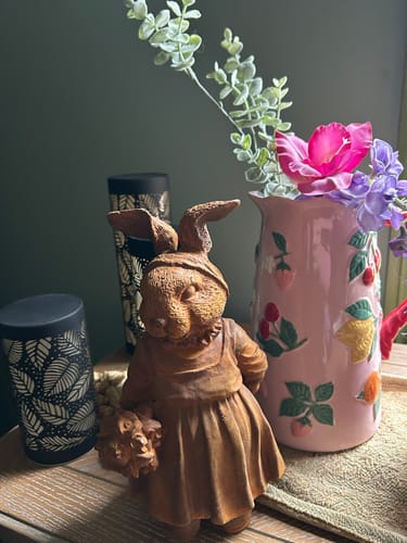 Customer's French Provincial rabbit statue displayed indoors on a table beside a pink floral jug.