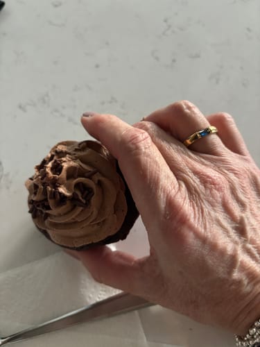 Customer's gold Treasure Birthstone Ring worn on a hand holding a chocolate cupcake