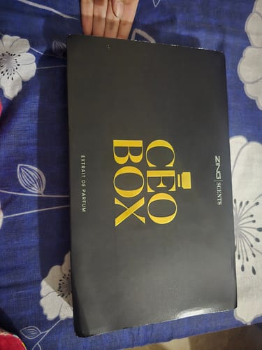 Customer's black Deal of the Month fragrance box with gold lettering on a floral patterned surface.