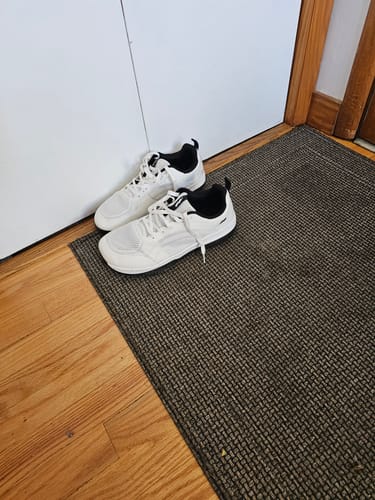 Customer's pair of white CUURT Muuv wide toe box court shoes on a dark mat indoors.