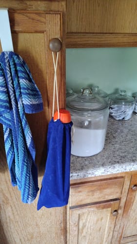 Customer's blue NovaCare Anti-Choking Device inside a storage bag hanging from a cabinet knob in a kitchen.