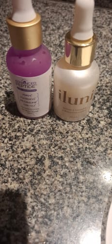 Customer's Advanced Peptide serum in a purple bottle standing next to another skincare product on a granite counter.