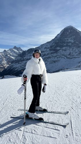 Reviewer in the white slim-fit ski suit with a faux fur jacket and flared pants on a mountain.