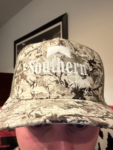 Customer showing a close-up of their Southern String camouflage hat with white embroidered text.