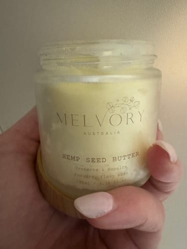 Reviewer's hand holding a clear jar of the thick, pale yellow Hemp Seed Butter.