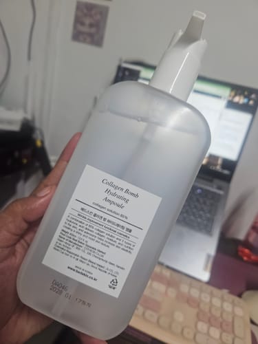 A customer holds up a large, frosted bottle of Bad Skin™ Korean Collagen Bomb Hydrating Ampoule.