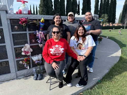 Reviewer wearing the red Paz y Amor sweatshirt, sitting with four other people at an outdoor memorial.