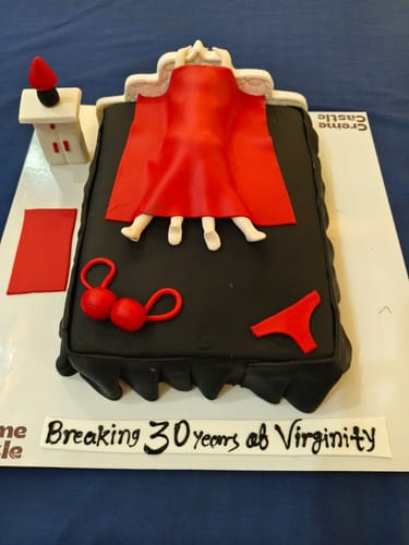 Reviewer's custom Night in Bed Cake with a couple under a red sheet and text 'Breaking 30 years of Virginity'.