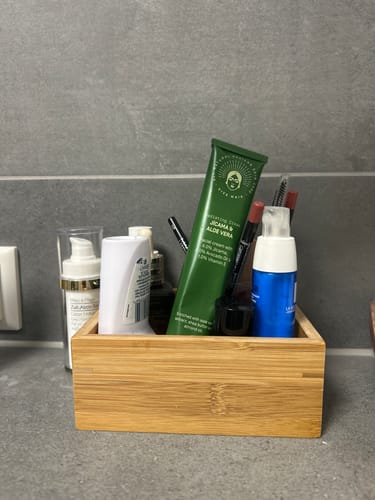 Customer's Radiating Cream in its green tube, placed in a wooden organizer with other toiletries on a counter.