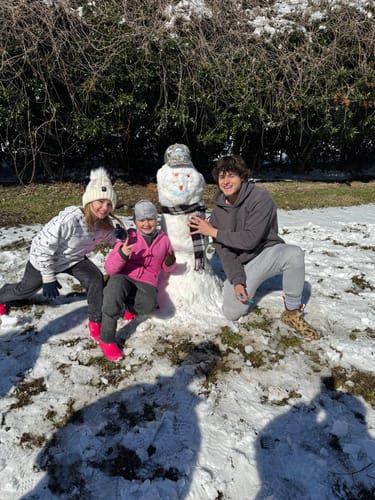 Customer photo of three people posing with a snowman wearing a patterned Hat of the Month Crew hat.