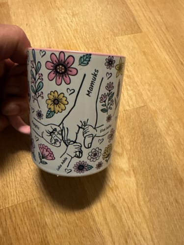 Kundens Kärleksmugg med ett personligt tryck av händer och färgglada blommor, sedd på nära håll.