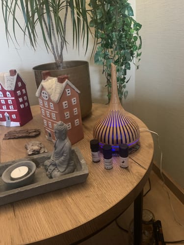Recensent toont de Yin etherische olie op een houten tafel naast een verlichte diffuser in een rustgevende setting.
