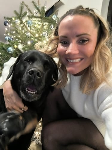 Une cliente sourit en serrant dans ses bras son chien noir heureux, qui prend le Complément articulations.