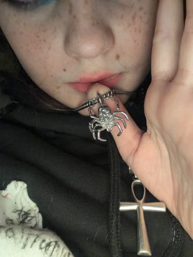 Close-up: Reviewer holding the shiny Spider Skull Pendant on its chain near their mouth.