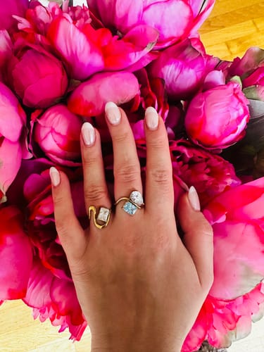 Reviewer showing the gold Sonata Ring on their hand, worn next to another ring over pink flowers.