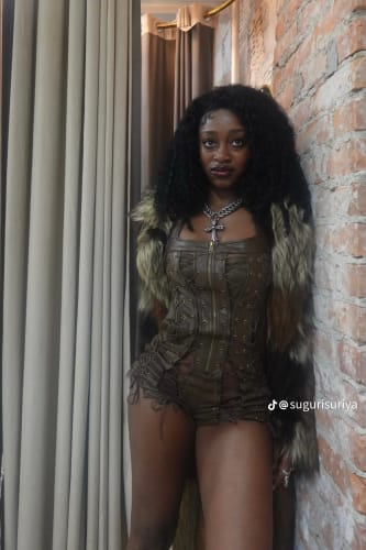 Reviewer posing in the dark Vice Body bodysuit, styled with a fur coat and standing next to a brick wall.