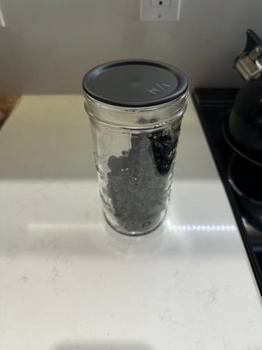 Customer's black chalkboard top mason jar lid on a glass jar filled with dark food, sitting on a kitchen counter.