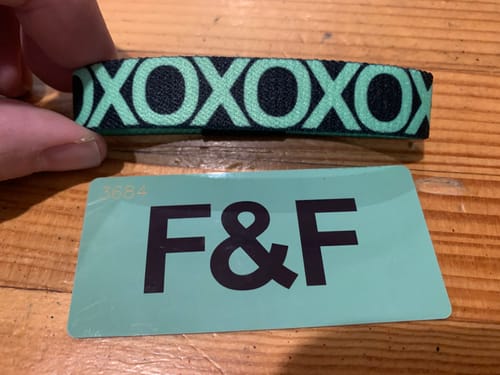 Customer holding the F&F Colorwheel Bracelet showing the black 'XOXO' pattern on a green background with its matching card.