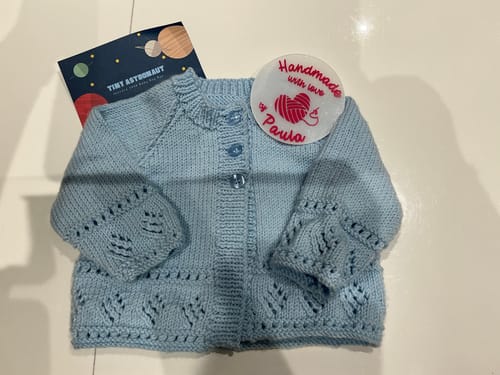 Reviewer's finished light blue baby cardigan, showing the detailed lacy pattern from the knit box.