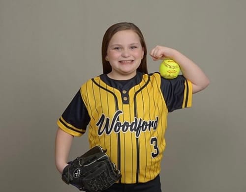 Customer smiling while wearing their custom gold and black striped softball jersey, holding a glove and softball.