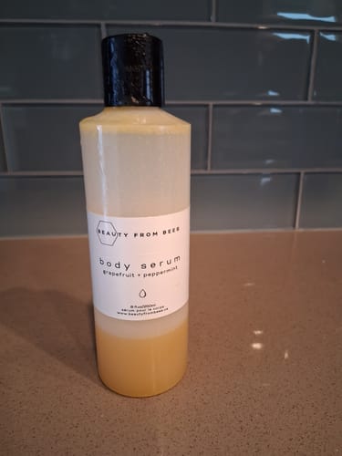 Customer's bottle of Body Serum in Grapefruit + Peppermint scent on a countertop, showing the liquid separated into two layers.