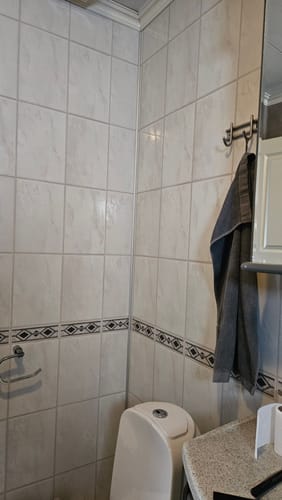 Kundes bilde av badet før oppussing, med hvite fliser og en mønstret bord på veggen.