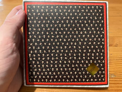 Customer holding the packaging for the Keep Smiling Scarf, a square box with a skull pattern.