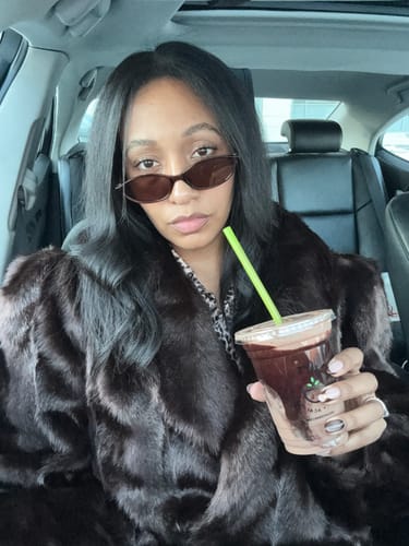 Reviewer wearing the dark Faux Mink Long Coat while sitting inside a car and holding a drink.