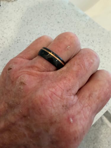 Close-up of a customer wearing The Direwolf ring, showing the black Damascus steel and rose gold inlay on their finger.