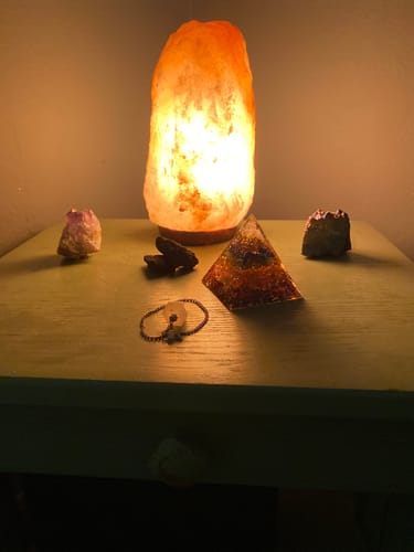 Reviewer's 7 Chakra Energy Pyramid displayed on a table with a glowing salt lamp and other crystals.