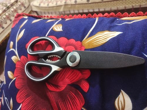 Customer's black kitchen scissor with its blade cover on, resting on a floral cushion.