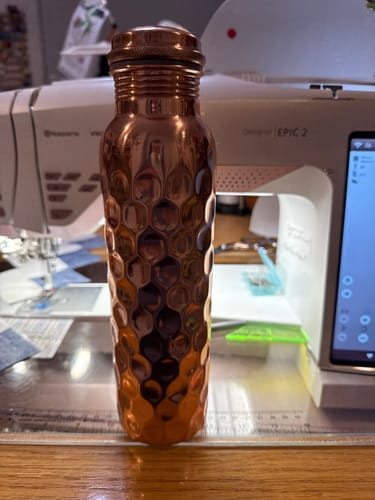 Customer's copper water bottle with a textured honeycomb design standing on a desk.