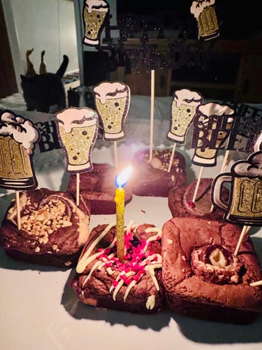 Customer's birthday brownies arranged with festive toppers and a single lit candle in one square.