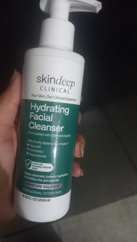 Customer holding the white and green pump bottle of Hydrating Facial Cleanser.