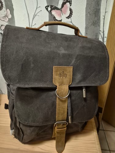 Ein Kunde zeigt seinen dunkelgrauen Daypack Acadia - Natura Rucksack auf einem Holzstuhl.