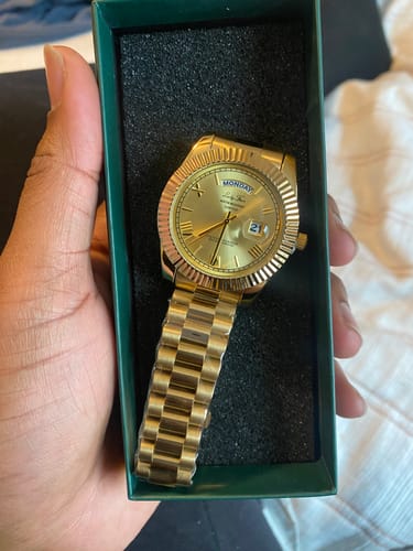 Reviewer holding an open green box, showing the gold-colored Lucky Fours® Santos watch on a black cushion.