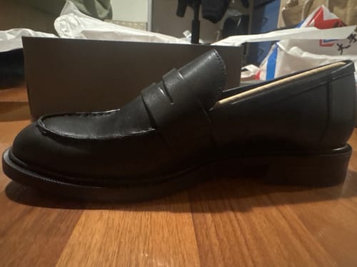 לקוחה מציגה נעל אוקספורד שחורה וקלאסית מדגם Vagabond Amina על רצפת עץ.