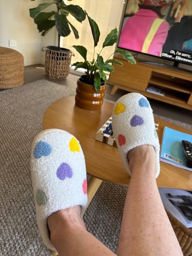 Reviewer relaxing with their feet up, wearing the plush Zia Colorful Heart Slippers.