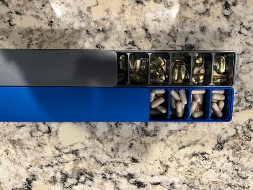 Customer's gray and blue Weekly AM-PM Vitamin XL Cases open on a counter, filled with pills.