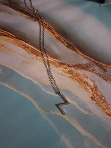 Un client montre le collier Rune Sōwilō de couleur argentée avec son pendentif en forme d'éclair.