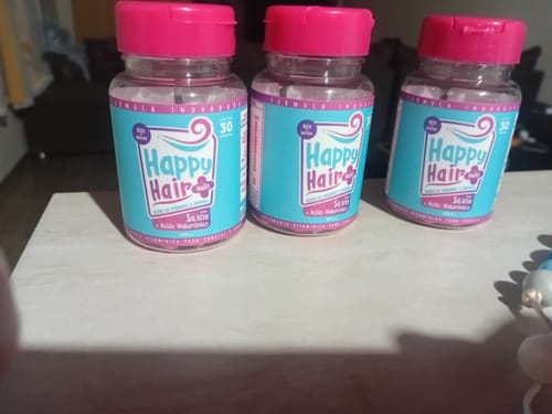 Cliente mostrando os três potes do suplemento Happy Hair sobre uma mesa.
