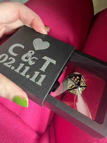 Customer holding a customized black box with engraved initials and a date, revealing a matching Dungeons & Dragons die inside.