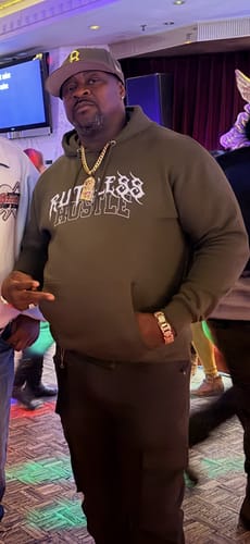 Customer posing indoors wearing a dark olive Play For Keeps Hoodie and dark pants.