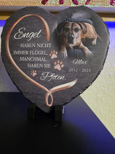 Ein Kunde zeigt sein individuelles Schieferherz mit einem Foto seines Hundes Max als Andenken auf einer Vitrine.