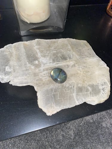 Reviewer's new monthly crystal, a polished iridescent stone, displayed on a larger white crystal slab.