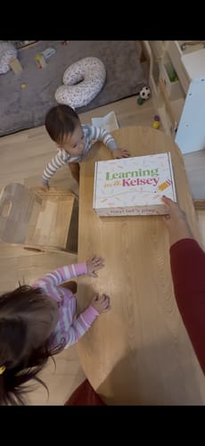 Customer placing the 'Learning with Kelsey' Toddler Box on a table in front of two curious toddlers.